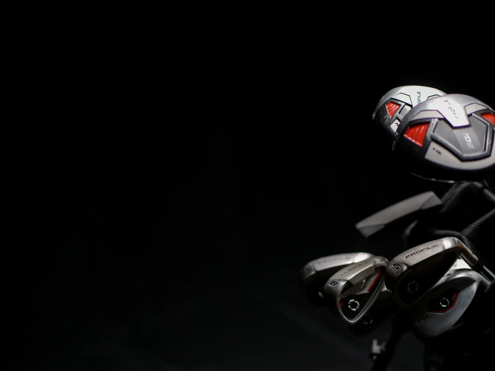 Artistic close-up image of modern golf clubs with dramatic lighting on the club heads.